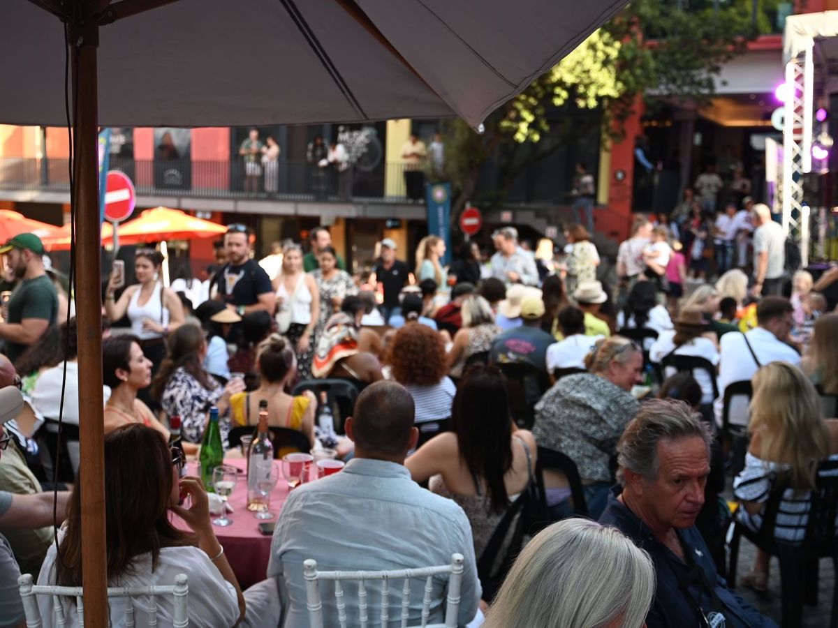 Crowds seated under umbrellas as the light drops in the late afternoon