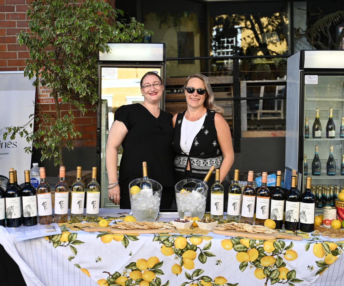 Two wine producers pouring behind a table lined with bottles at their festival stand